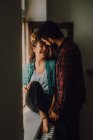 Joyful casual couple smiling and hugging while leaning on window sill — Stock Photo