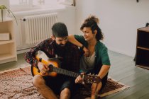 Веселые мужчина и женщина в повседневных нарядах играют на гитаре дома — стоковое фото