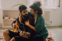 Allegro uomo e donna in abiti casual suonare la chitarra a casa — Foto stock