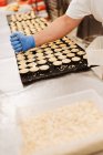 Cocinero anónimo exprimiendo masa de pastelería fresca en bandeja con papel - foto de stock