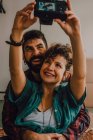 Cariñosa pareja hipster abrazando y tomando selfie en la cámara mientras está sentado en el suelo en casa - foto de stock