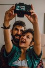 Liebevolles Hipster-Paar umarmt sich und macht Selfie mit Kamera, während es zu Hause auf dem Boden sitzt — Stockfoto