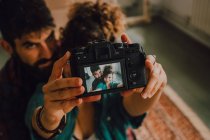 De cima vista do casal hipster afetuoso abraçando e tirando selfie na câmera enquanto sentado em casa — Fotografia de Stock