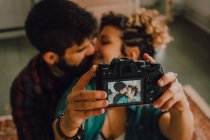 De cima vista do casal hipster afetuoso abraçando e tirando selfie na câmera enquanto sentado em casa — Fotografia de Stock