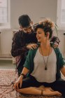 Uomo in abbigliamento casual massaggiare spalle di donna rilassata seduta in posizione loto sul pavimento a casa — Foto stock