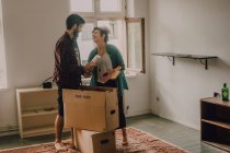 Couple hipster déballer ensemble des boîtes tout en se tenant pieds nus dans la pièce lumineuse — Photo de stock