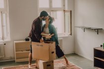 Hipster coppia disimballaggio insieme scatole mentre in piedi a piedi nudi in camera luce e baci — Foto stock
