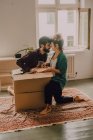 Alegre pareja riendo mientras se sienta al lado de cajas de cartón abiertas en apartamento moderno - foto de stock