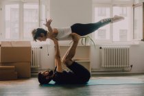 Vista lateral de pareja atlética ejercitando y equilibrando juntos en el piso en apartamento moderno - foto de stock