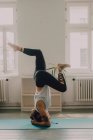 Vista laterale della donna in activewear che esercita e fa headstand sul pavimento in appartamento — Foto stock