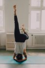 Vista posteriore della donna in activewear che esercita e fa headstand sul pavimento in appartamento — Foto stock