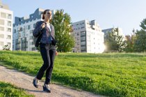 Empresária de comprimento total com saco andando ao longo do caminho perto do gramado verde no dia ensolarado no parque da cidade — Fotografia de Stock