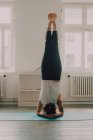 Visão traseira da mulher em activewear exercitando e fazendo headstand no chão no apartamento — Fotografia de Stock