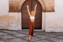 Приваблива молода жінка в стильному вбранні танцює з закритими очима на стародавній будівлі з бурхливими воротами на вулиці старого міста — стокове фото