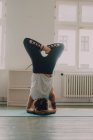 Задний вид на женщину в активной спортивной и делать стойку на голове на полу в квартире — стоковое фото