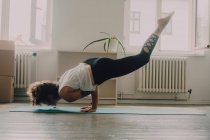 Вид сбоку гибкой женщины в верхней одежде, выполняющей упражнения и стоящей на руках на полу в квартире — стоковое фото
