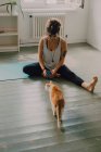 Fürsorgliche Gelegenheitsfrau gibt neugierigen Katzen Futter, während sie barfuß in einer minimalistischen modernen Wohnung sitzt — Stockfoto
