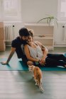 Vista laterale della coppia tenera che si abbraccia mentre si siede sul pavimento accanto al gatto rossiccio a casa — Foto stock