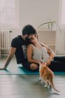 Вид збоку ніжної пари, що обіймає і цілує, сидячи на підлозі поруч з імбирним котом вдома — стокове фото