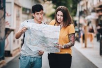 Позитивный смех мультиэтнических людей, ищущих направление на карте стоя на городской улице — стоковое фото