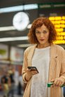 Червоне волосся молода жінка використовує смартфон на станції — стокове фото