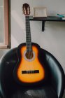 Современная акустическая гитара на минималистском круглом стуле по белой стене с полкой дома — стоковое фото