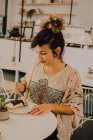Fröhliche, lässige Frau isst Kuchen mit Gabel, während sie am Tisch in der Cafeteria sitzt — Stockfoto