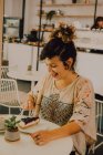Joyful mulher casual comer bolo com garfo enquanto sentado à mesa na cafetaria — Fotografia de Stock