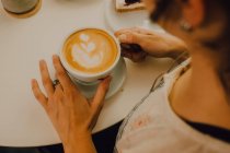 Vista in prima persona della donna che tiene la tazza mentre è seduta nella moderna caffetteria — Foto stock
