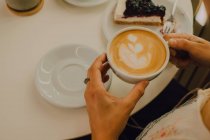 Vista en primera persona de la mujer sosteniendo taza mientras está sentado en la cafetería moderna - foto de stock