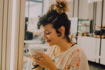 Vista lateral da mulher sorridente feliz cheirando caneca enquanto sentado em café moderno — Fotografia de Stock