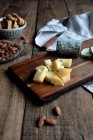Сладкие гренки с изюмом и тарелка с миндалем помещены на деревянный стол рядом с доской с разнообразным сыром — стоковое фото