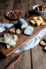Süße Croutons mit Rosinen und Teller mit Mandeln auf Holztisch neben Brett mit verschiedenen geschnittenen Käse platziert — Stockfoto