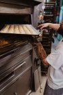 Crop man espreitando dentro do forno profissional enquanto trabalhava na padaria — Fotografia de Stock
