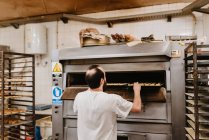 Homme regardant à l'intérieur four professionnel tout en travaillant dans la boulangerie — Photo de stock
