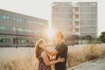 Vista lateral da ligação romântica casal na estrada ao longo do edifício urbano na luz solar — Fotografia de Stock