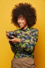 Професійний афроамериканський фотограф переглядає зображення на стильній фотокамері, стоячи на жовтому фоні. — стокове фото