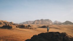 Mujer parada en la cima de la roca mirando Wadi Rum - foto de stock