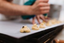 Cozinheiro anônimo espremendo massa de pastelaria fresca na bandeja com papel enquanto trabalhava no fundo borrado da padaria — Fotografia de Stock