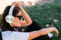 Donna pacifica con occhiali da sole e cuffie che ascolta musica mentre siede sull'erba nel parco — Foto stock