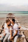 Glad lovers sitting on destroyed pier on seashore — Stock Photo