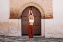 Attraktive junge Frau in stylischem Outfit tanzt mit geschlossenen Augen gegen ein altes Gebäude mit schäbigem Tor auf der Straße der Altstadt — Stockfoto