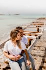 Verliebte sitzen auf zerstörter Seebrücke am Meeresufer — Stockfoto