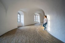 Lässige Frau lehnt an Wand in geräumiger Galerie mit Fenstern — Stockfoto