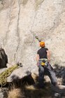 Escalador de roca con casco naranja está mirando a la cima de la montaña que va a subir - foto de stock