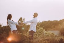 Side view of happy loving couple in matching casual clothes holding hands and looking at each other while standing at field — Stock Photo