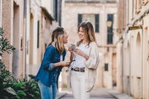 Молодые привлекательные улыбающиеся женщины ходят и общаются с мобильными телефонами на улице — стоковое фото