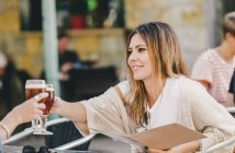 Mulher elegante atraente com copo de cerveja refrescante sentado no café e clinking com amigo — Fotografia de Stock