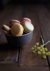 Yellow dill flowers placed on wooden table near bowl of fresh colorful macaroons — Stock Photo