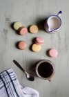 Draufsicht auf Dessertlöffel und Baumwolltuch in der Nähe einer Tasse frischen Kaffees, Milchkännchen und bunten Makronen auf weißem Tisch — Stockfoto